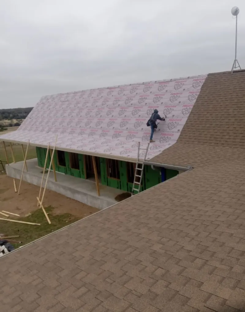 Worker preparing underlayment for a metal roof installation in Peculiar